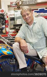 Portrait of senior man sitting on motorcycle in workshop