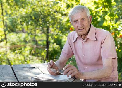 portrait of senior man sitting with glasses reading a newspaper at a table in the garden
