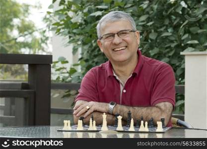 Portrait of senior man smiling while sitting by table with chess board