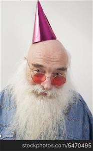 Portrait of senior man wearing red glasses and party hat over gray background