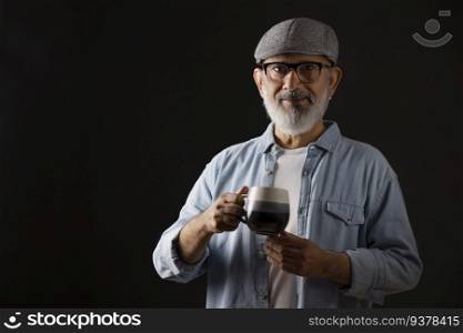 Portrait of senior man with flat cap holding a cup of coffee against dark background