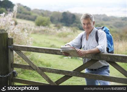 Portrait Of Senior Man With Map On Hike In Countryside Resting By Gate