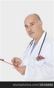 Portrait of senior medical practitioner with clipboard over gray background