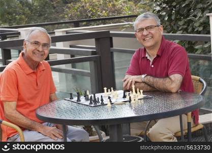Portrait of senior men smiling while sitting around table with chess board