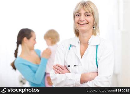 Portrait of senior pediatric doctor and mother with baby in background
