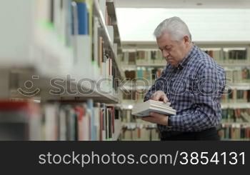 Portrait of senior retired man choosing book in library and taking it from shelf. Dolly shot