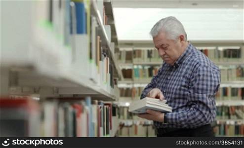 Portrait of senior retired man choosing book in library and taking it from shelf. Dolly shot