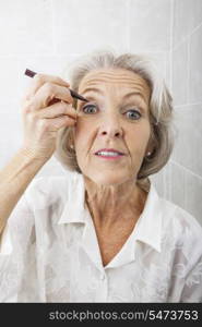 Portrait of senior woman applying eyeliner in bathroom