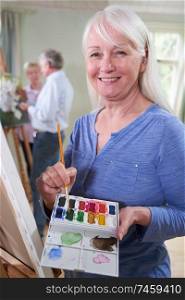 Portrait Of Senior Woman Attending Painting Class With Teacher In Background