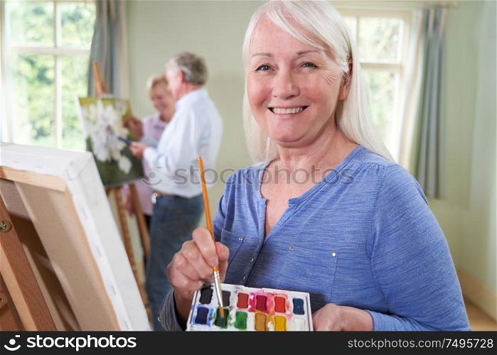 Portrait Of Senior Woman Attending Painting Class With Teacher In Background