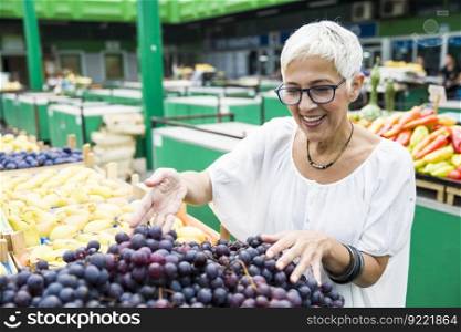 Portrait of senior woman chooses red grapes at the market