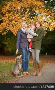 Portrait of senior woman, daughter, granddaughter and dog in autumn park