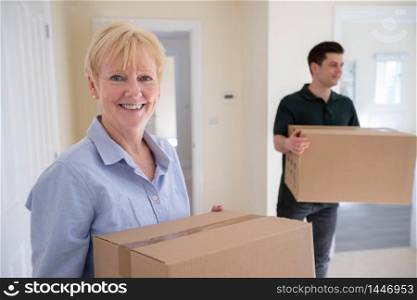 Portrait Of Senior Woman Downsizing In Retirement Carrying Boxes Into New Home On Moving Day With Removal Man Helping