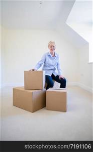 Portrait Of Senior Woman Downsizing In Retirement Sitting On Boxes In New Home On Moving Day