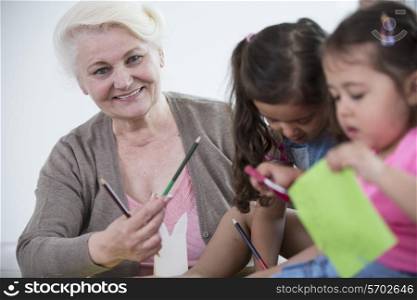 Portrait of senior woman helping granddaughters in making handicrafts at home