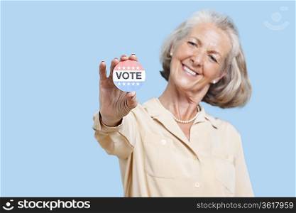 Portrait of senior woman holding an election badge against blue background