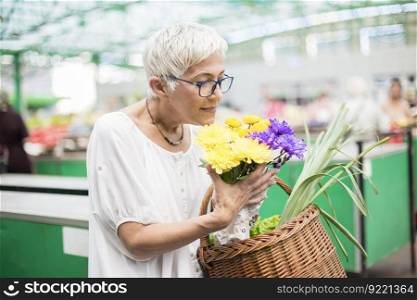 Portrait of senior woman holding basket with bouquet of flowers on market