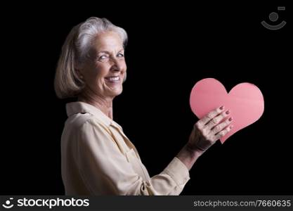 Portrait of senior woman holding red heart shaped paper in studio