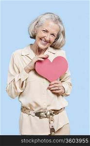Portrait of senior woman holding red paper heart against blue background