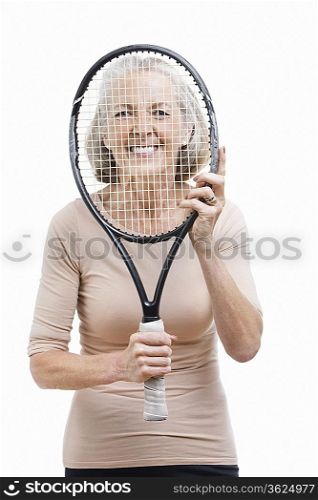 Portrait of senior woman holding tennis racket in front of her face against white background
