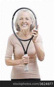 Portrait of senior woman holding tennis racket in front of her face against white background