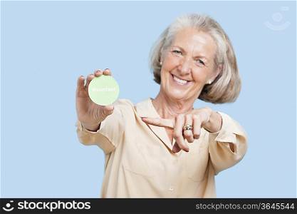 Portrait of senior woman holding volunteer badge against blue background
