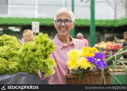 Portrait of senior woman holds basket with flowers and  buys lettuce on market