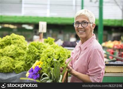 Portrait of senior woman holds basket with flowers and  buys lettuce on market