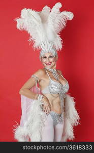 Portrait of senior woman in showgirl&acute;s outfit and feather headpiece over red background