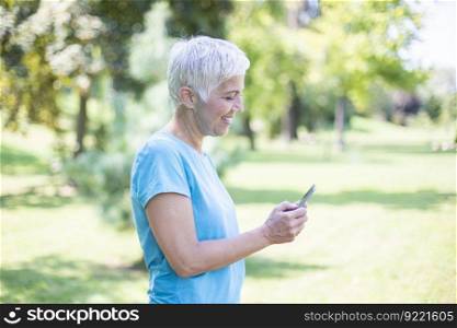 Portrait of senior woman in sports clothing  using smart phone outdoor