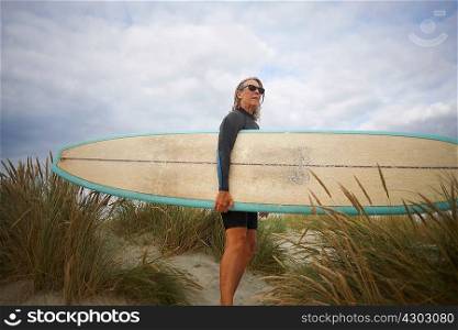 Portrait of senior woman on sand, holding surfboard