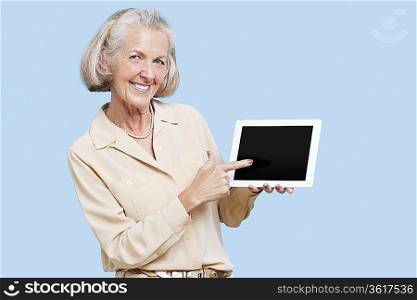 Portrait of senior woman showing tablet PC against blue background