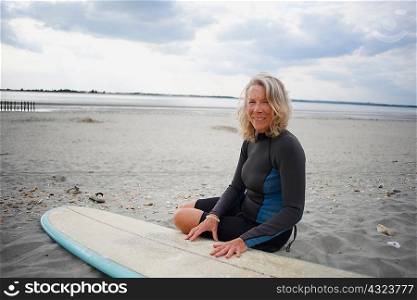 Portrait of senior woman sitting on beach next to surfboard