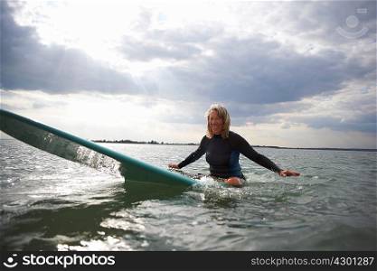 Portrait of senior woman sitting on surfboard in sea, smiling