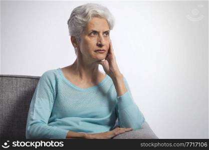 Portrait of senior woman thinking sitting on sofa with hand on chin