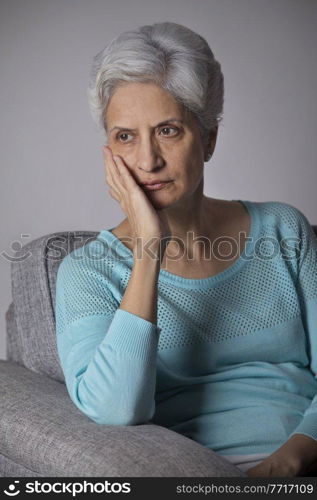 Portrait of senior woman thinking sitting on sofa with hand on chin