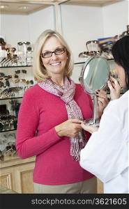 Portrait of senior woman wearing glasses while optician holding mirror