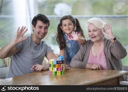 Portrait of senior woman with son and granddaughter waving hands at table
