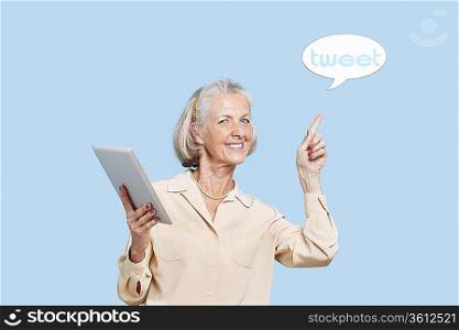 Portrait of senior woman with tablet PC pointing at tweet bubble against blue background