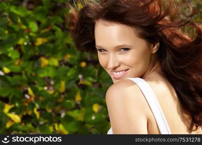 Portrait of sensual beauty with flying hair against green foliage