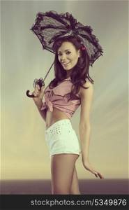 portrait of sensual brunette girl posing like pin-up with lace parasol and wearing white shorts and shirt. Smiling and looking in camera
