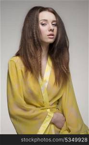 portrait of sensual brunette girl with long hair wearing yellow transparent nightgown and looking in camera