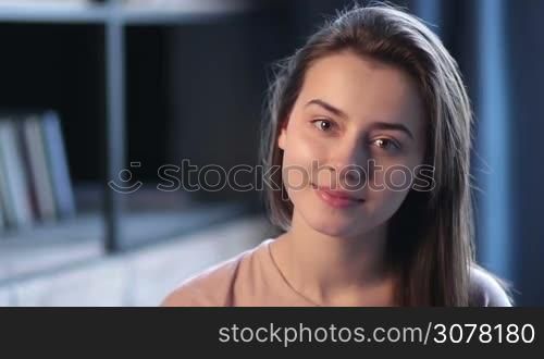 Portrait of sensual cute brunettte girl with deep grey eyes looking at the camera with perfect smile and white teeth in home interior. Affectionate young woman smiling with innocent smile. Slow motion.