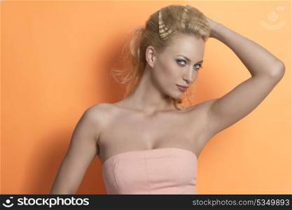 portrait of sensual woman with blond creative hair-style, colorful make-up and pink dress in fashion pose on orange background