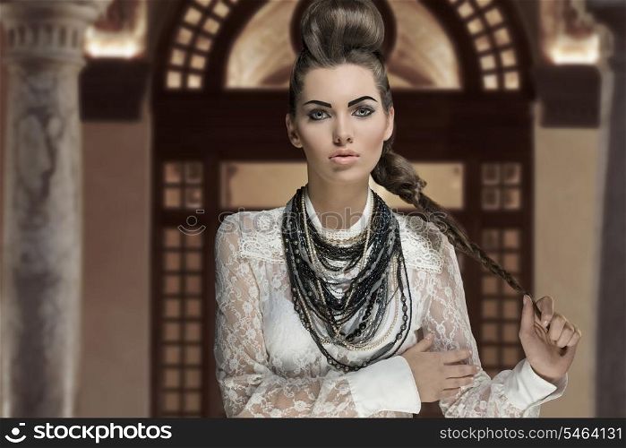 portrait of sensual young brunette woman with creative fashion style and cute hairdo and make-up. Wearing white lace shirt and a lot of necklaces