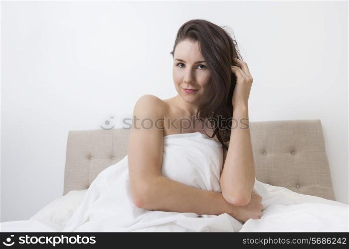 Portrait of sensuous woman covered with bedsheet in bed