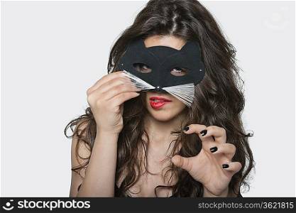 Portrait of sensuous young woman wearing cat mask while biting lip over gray background
