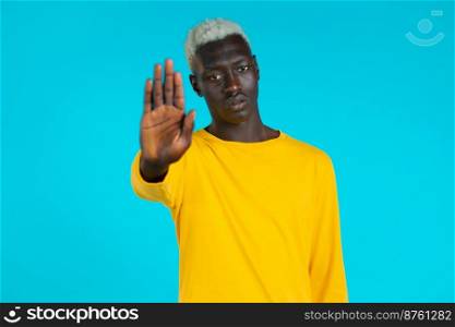 Portrait of serious african american man showing rejecting gesture by stop palm sign. Guy isolated on blue background. Portrait of serious african american man showing rejecting gesture by stop palm sign. Guy isolated on blue background.