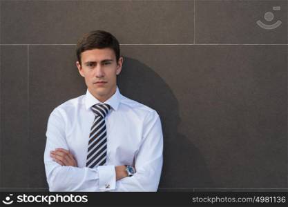 Portrait of serious and confident adult businessman wearing shirt and necktie with arms crossed in front of gray wall with copyspace