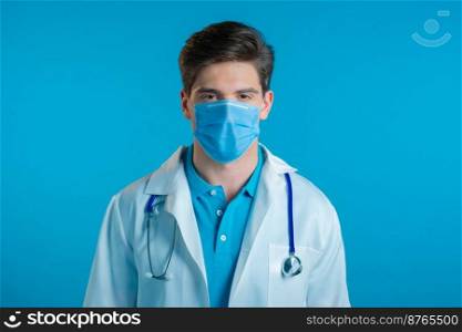 Portrait of serious doctor in professional medical mask and coat. Doc man isolated on blue background. High quality photo. Portrait of serious doctor in professional medical mask and coat. Doc man isolated on blue background.